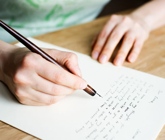 An image of a person hand writing on a paper with a caligraphy pen